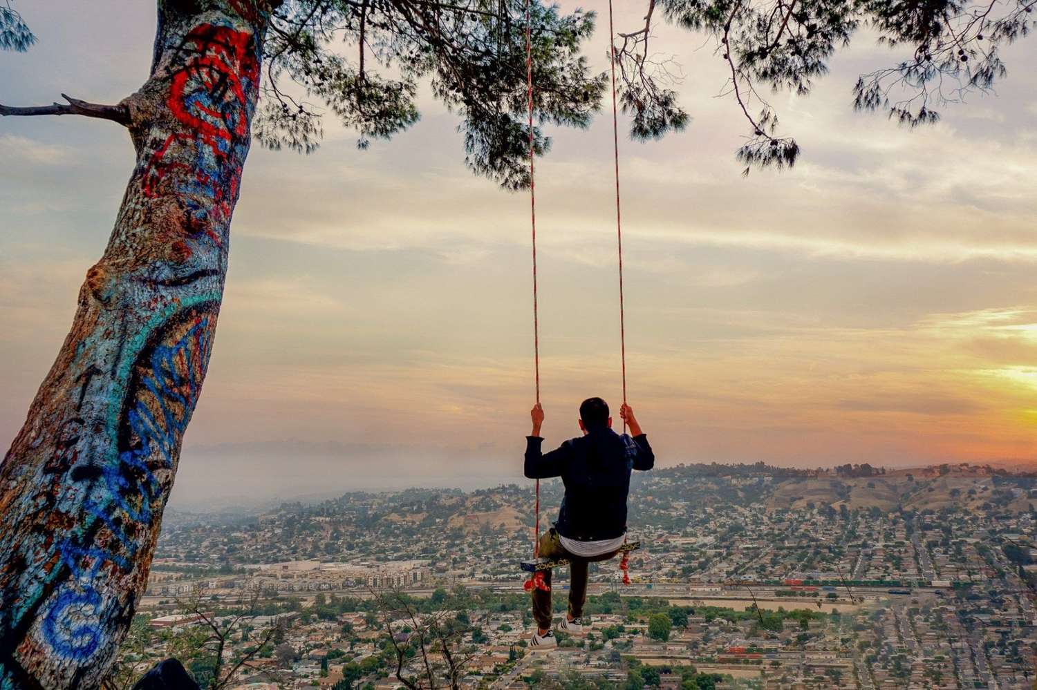 Man swinging on Elysian Park Swing at sunset with a panoramic view of Los Angeles below.