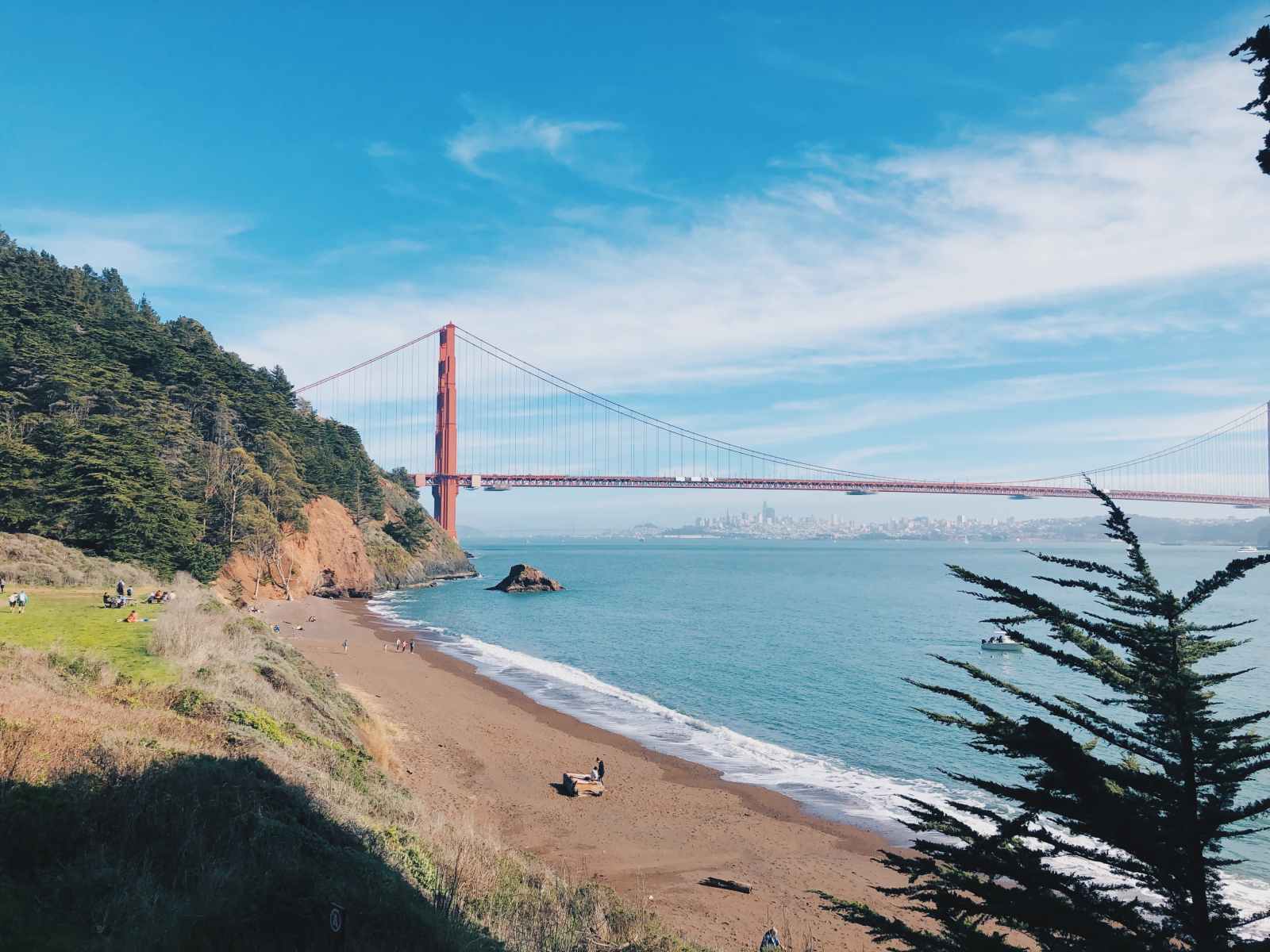 View of Kirby Cove Beach with the Golden Gate Bridge in the background and a shoreline bordered by trees and rocky cliffs.