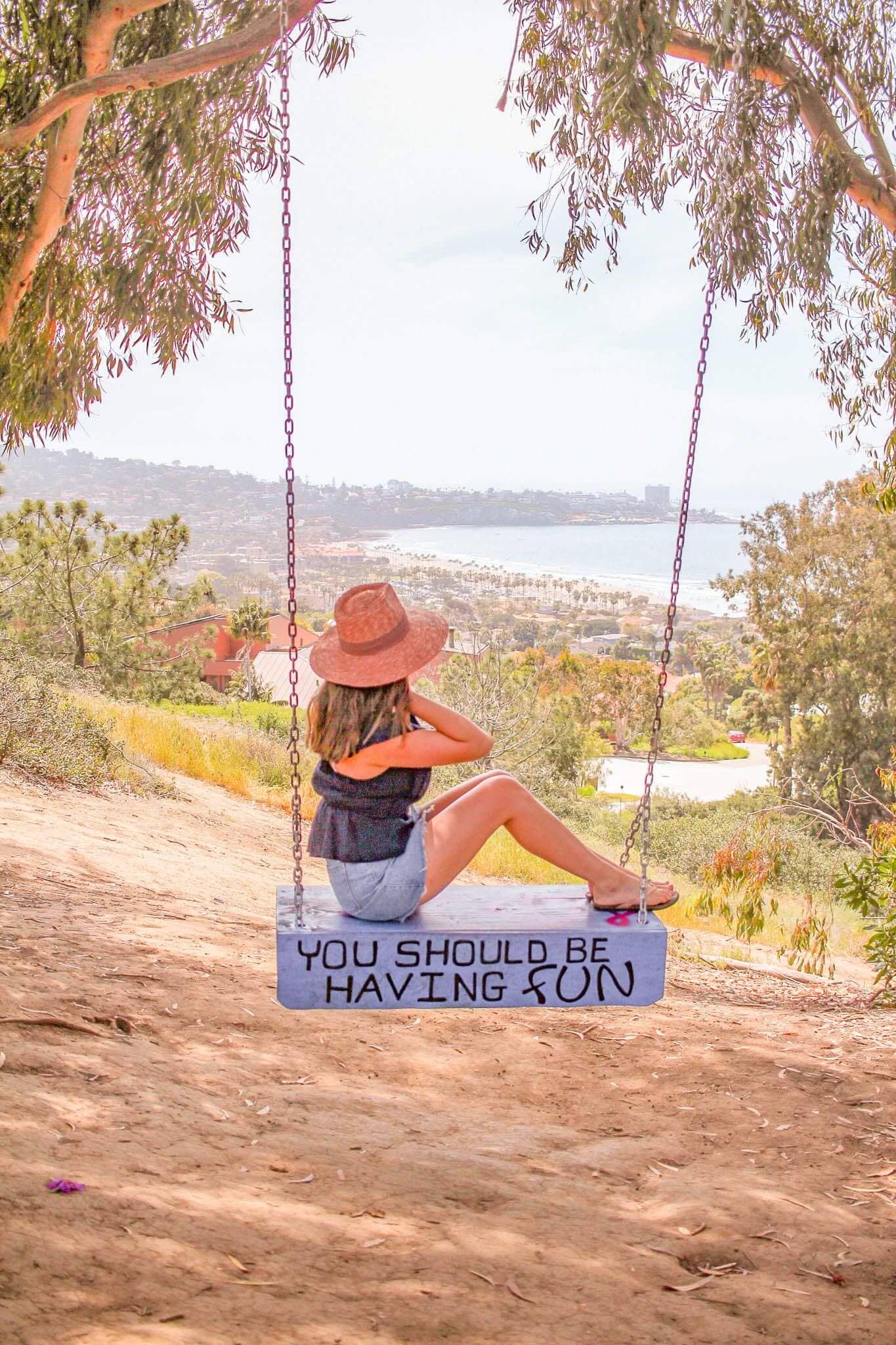 Woman in an orange hat sitting on La Jolla Swing with quote "You should be having fun" and enjoying nice view. 