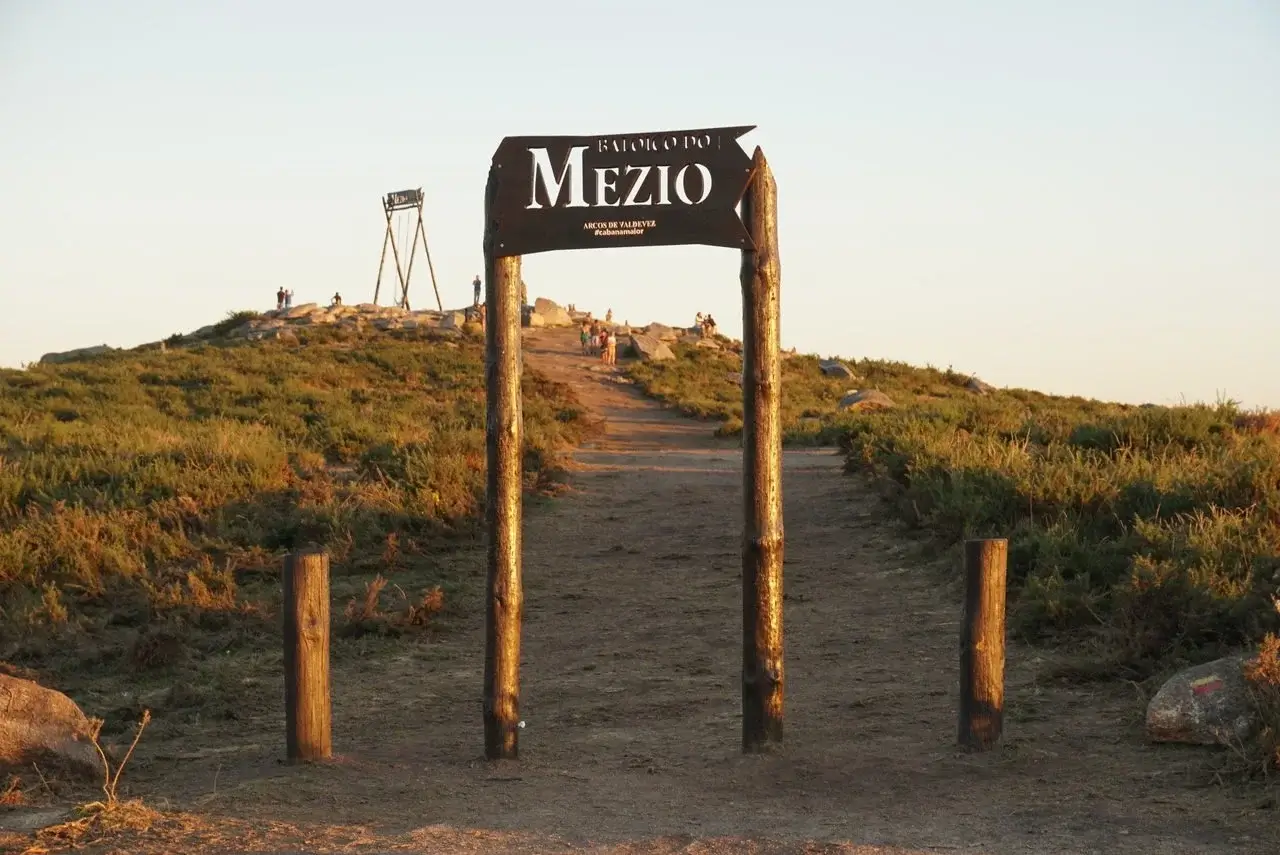 A dirt path leads to the Baloico do Mezio swing, visible in the distance, set atop a hill in a scenic landscape with golden light during sunset.