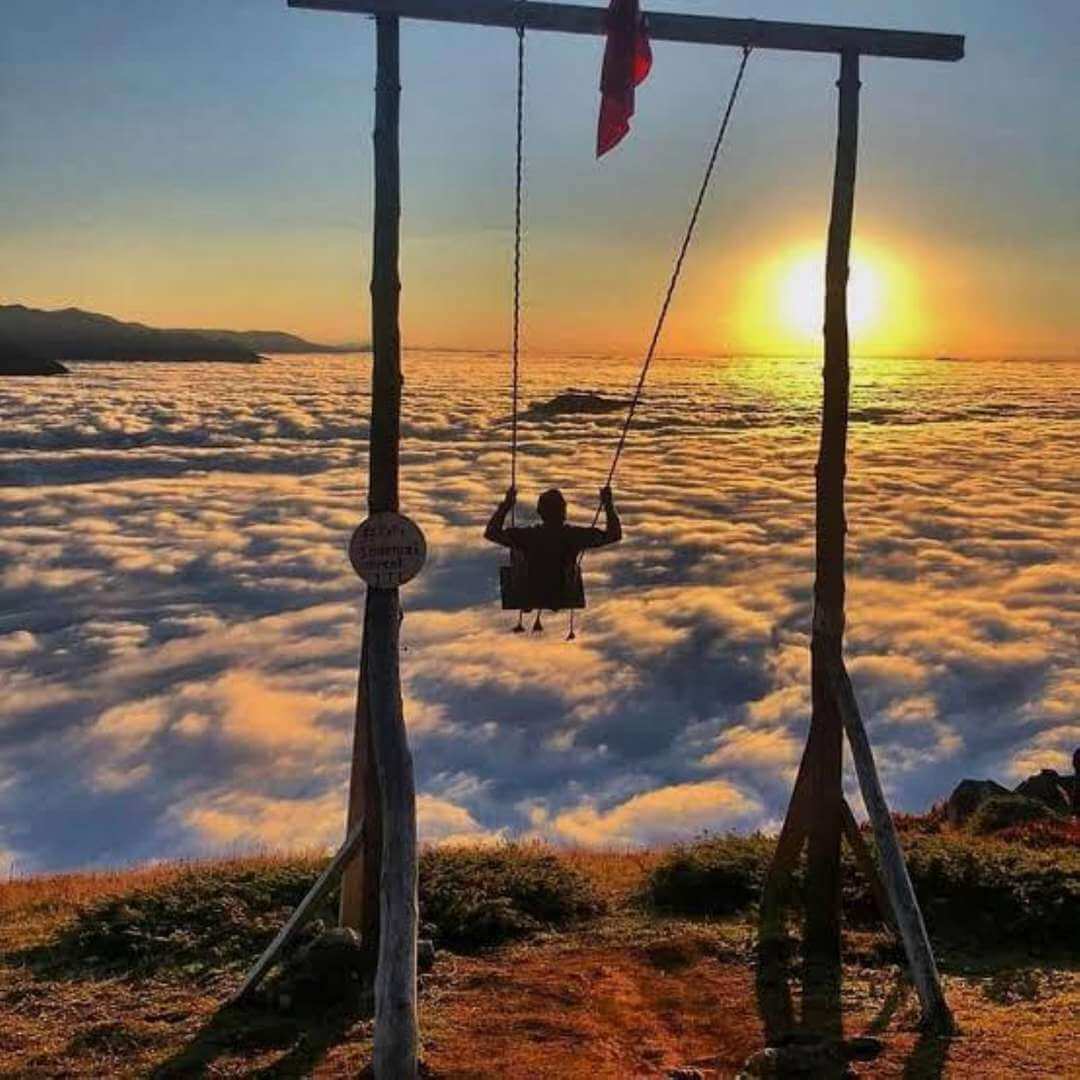 A person swings above clouds at sunset, with a stunning golden sky in the background.