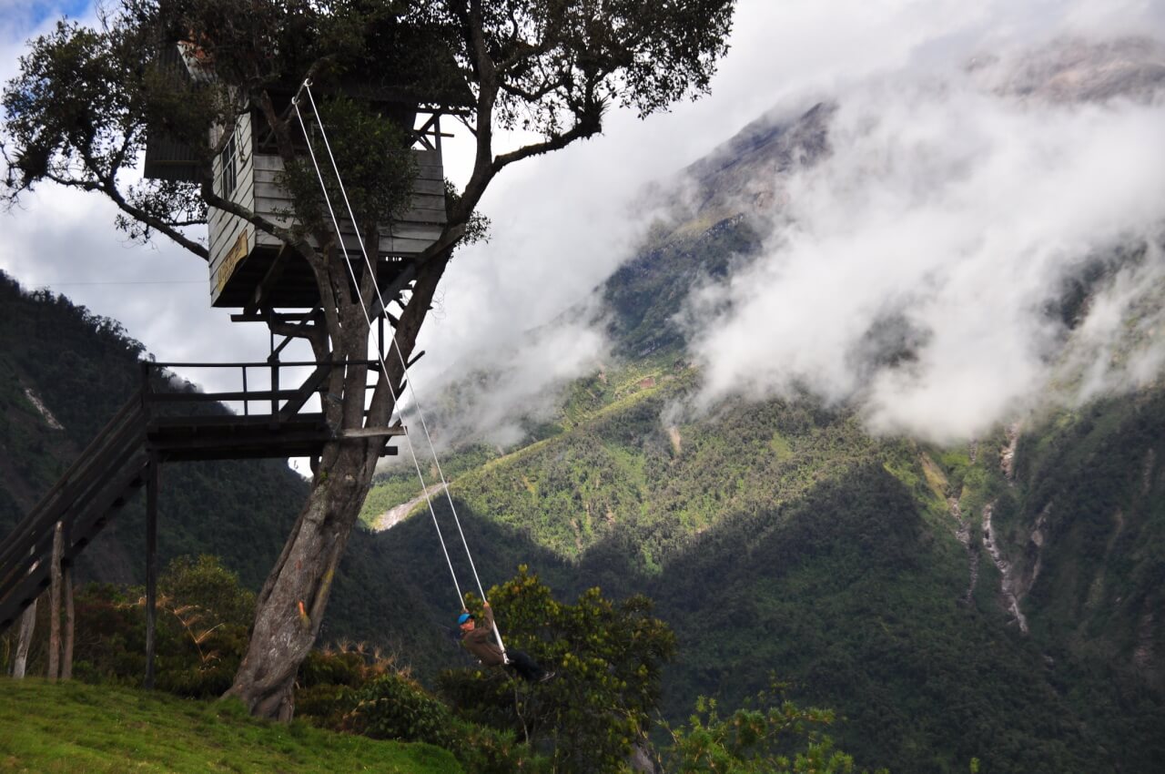 A wooden treehouse with a rope swing attached to it, overlooking a foggy mountain landscape.